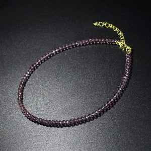 Blue faceted glass bead choker necklace with a gold tone clasp laid in a circle