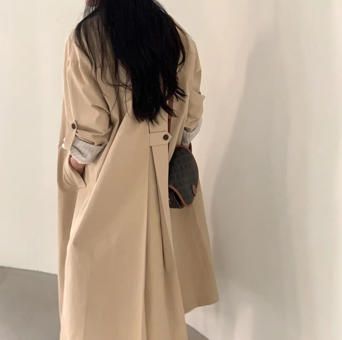 Back of the light khaki long trench coat showing the loose drape and back waist tab