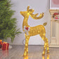 Golden lit reindeer with its head turned back and a silver bow with red berries beside a Christmas tree and gifts