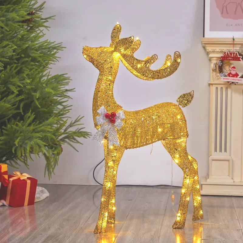 Golden lit reindeer with its head turned back and a silver bow with red berries beside a Christmas tree and gifts