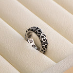 Silver gray scrollwork band ring with engraved gothic lettering inside, resting in a cream leather ring tray