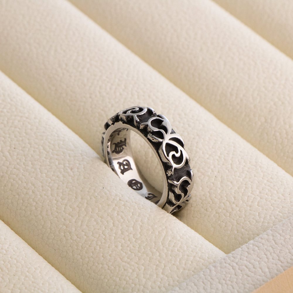 Silver gray scrollwork band ring with engraved gothic lettering inside, resting in a cream leather ring tray