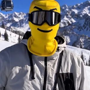 Yellow block head printed face cover with a smile and ski goggles on a snowy mountain, front view