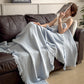 Sky Blue cotton gauze throw blanket with tassel fringe, draped over a seated woman on a dark leather sofa, view 4 of 4