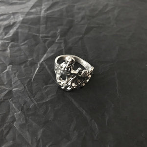 Molten texture steel ring resting on dark crumpled paper, raised ridges and darkened recesses in the relief