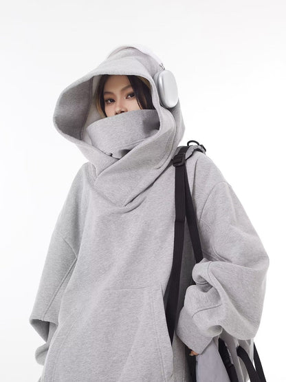 Grey oversized hooded sweatshirt with the high collar and hood pulled up, worn with white headphones and a shoulder bag