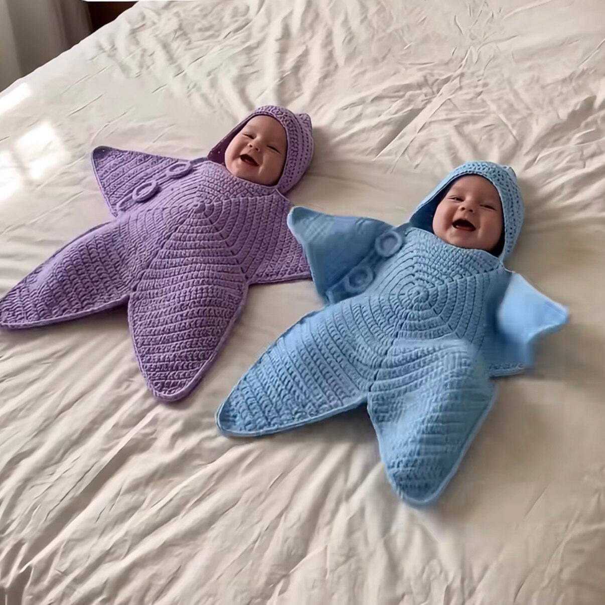 Purple and blue crochet star-shaped baby buntings worn by two babies lying on a bed
