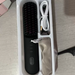 Black cordless straightening comb with a white USB charging cable shown inside the open retail box tray