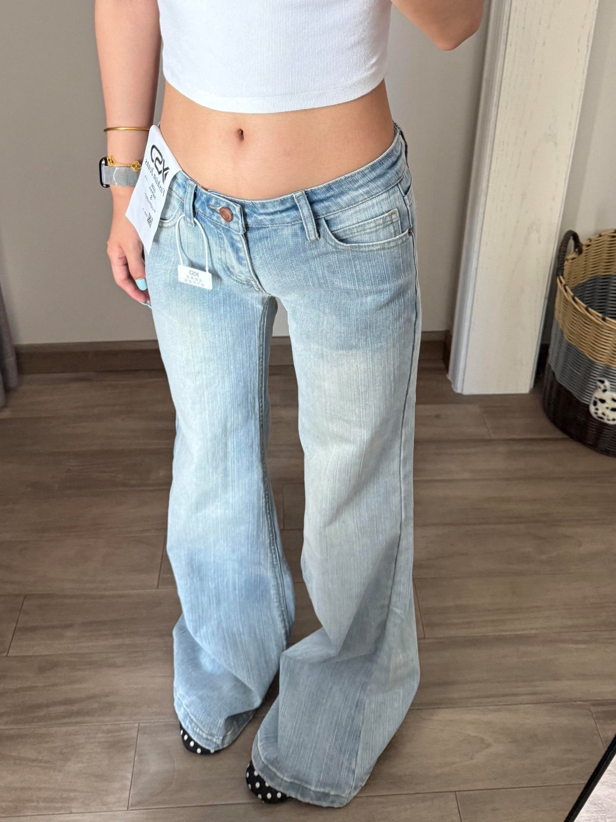 Woman wearing low rise light wash flared jeans with a white crop top, front view in a mirror