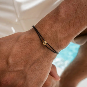 Thin black cord lucky charm bracelet with a small gold charm worn on a mans wrist