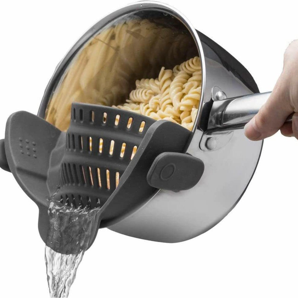 Dark gray silicone clip-on pot strainer, variant photo, clipped to a pot held by hand with water draining