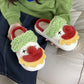Pair of clown face plush slippers resting on a lap showing the open back, red trim and beige plush lining