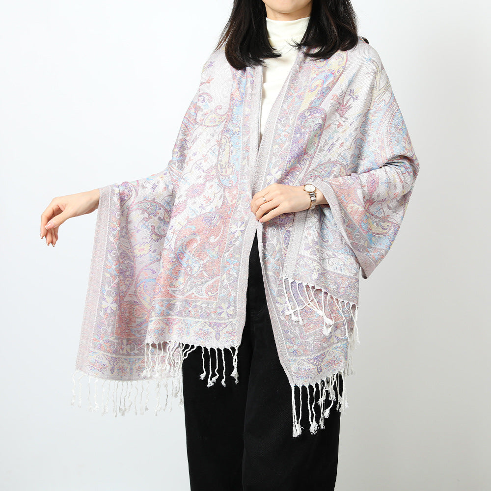 Woman wearing an ivory paisley jacquard scarf draped over both shoulders with white tassel fringe