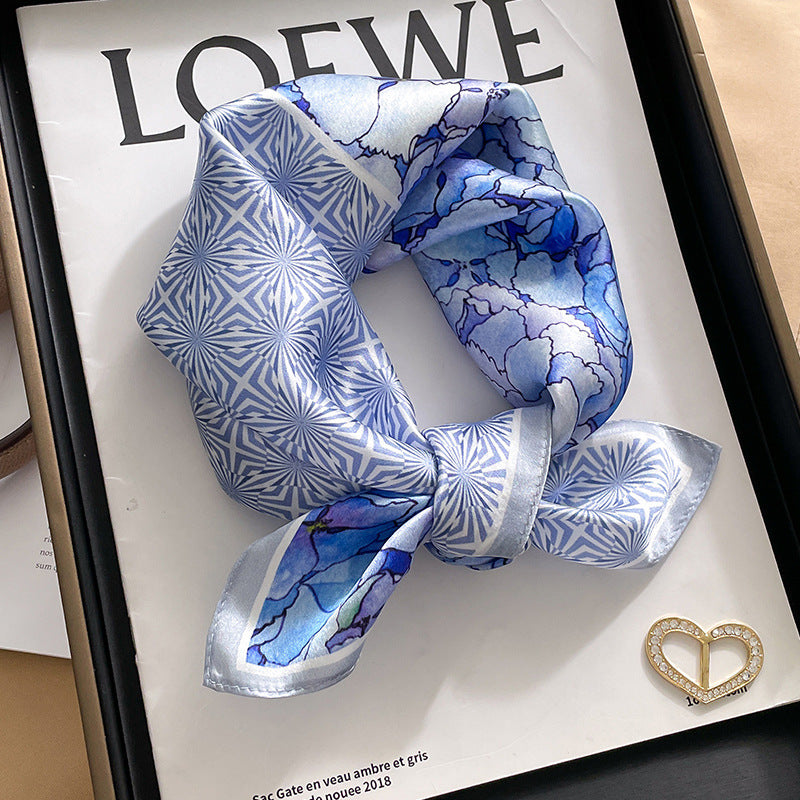 Light blue geometric printed square scarf with a satin sheen and hemmed edges, shown displayed