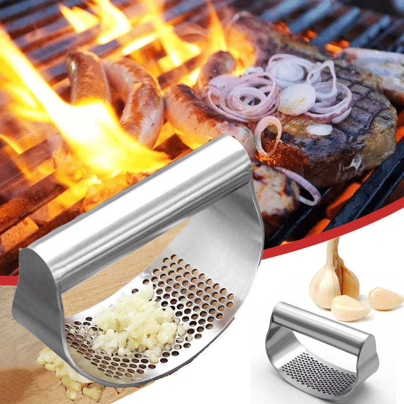 Stainless steel rocking garlic press with minced garlic on a board beside garlic bulbs
