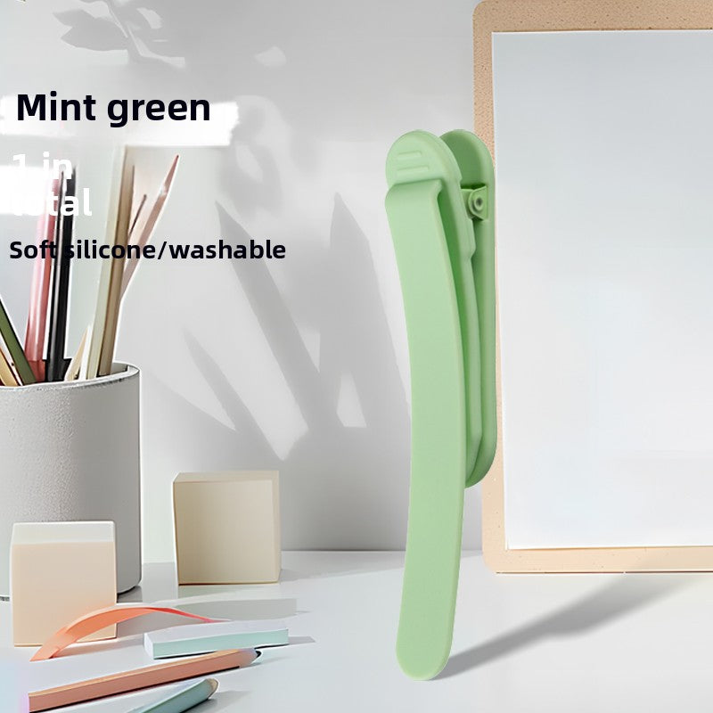 Single mint green silicone bookmark clip standing on a desk beside a pen cup