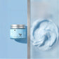 Open tin of pale blue whipped tallow balm next to a swirl of the airy blue moisturizer on a matching backdrop