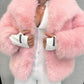 Pink vegan fur jacket worn open over a white outfit with white cuffs showing at the sleeves