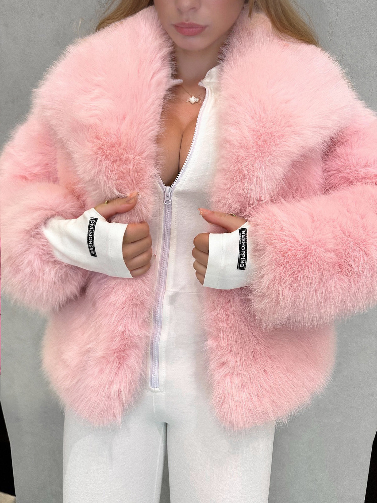 Pink vegan fur jacket worn open over a white outfit with white cuffs showing at the sleeves
