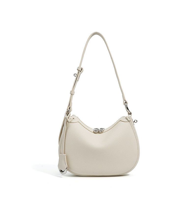Off white pebbled leather crescent bag with a long adjustable shoulder strap and metal tipped leather tab