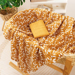 Cotton muslin gauze baby blanket in mustard botanical print draped over a nursery rocking chair