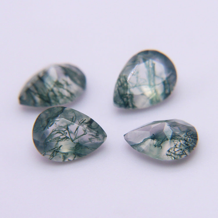 Four pear cut moss agate stones on a pale grey surface, green dendrites under faceted crowns