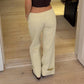 Back view of beige wide leg trousers with a folded cuff hem on a model standing on a wooden floor