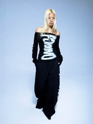 Full length view of the black graphic top styled with wide black trousers on a blue backdrop