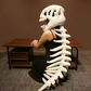 White plush dinosaur skeleton head mask worn while kneeling, long spine trailing behind