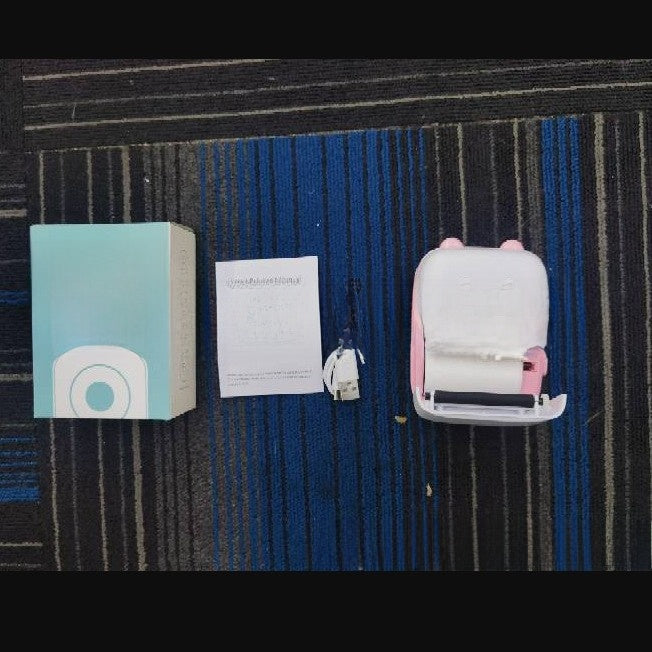 Top view of a box, paper roll, cable and a pink cat ear thermal printer on a dark mat, C9 pink option