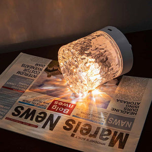 Rippled acrylic lamp shade with a white base glowing warm white on a newspaper