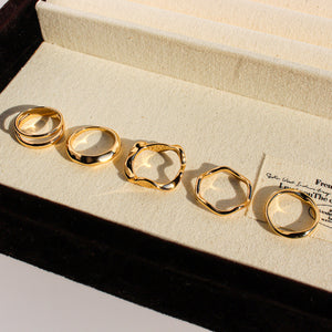 Five gold rings lined up inside a cream jewelry display box