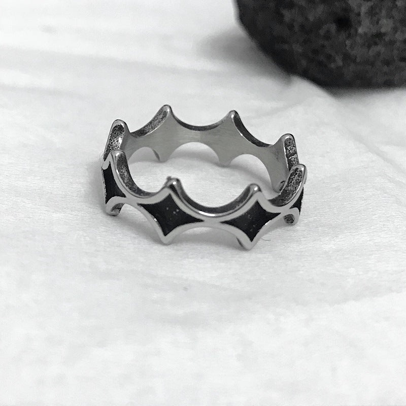Steel band ring with blackened diamond pattern resting on white fabric beside a dark lava rock