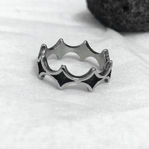 Steel band ring with blackened diamond pattern resting on white fabric beside a dark lava rock