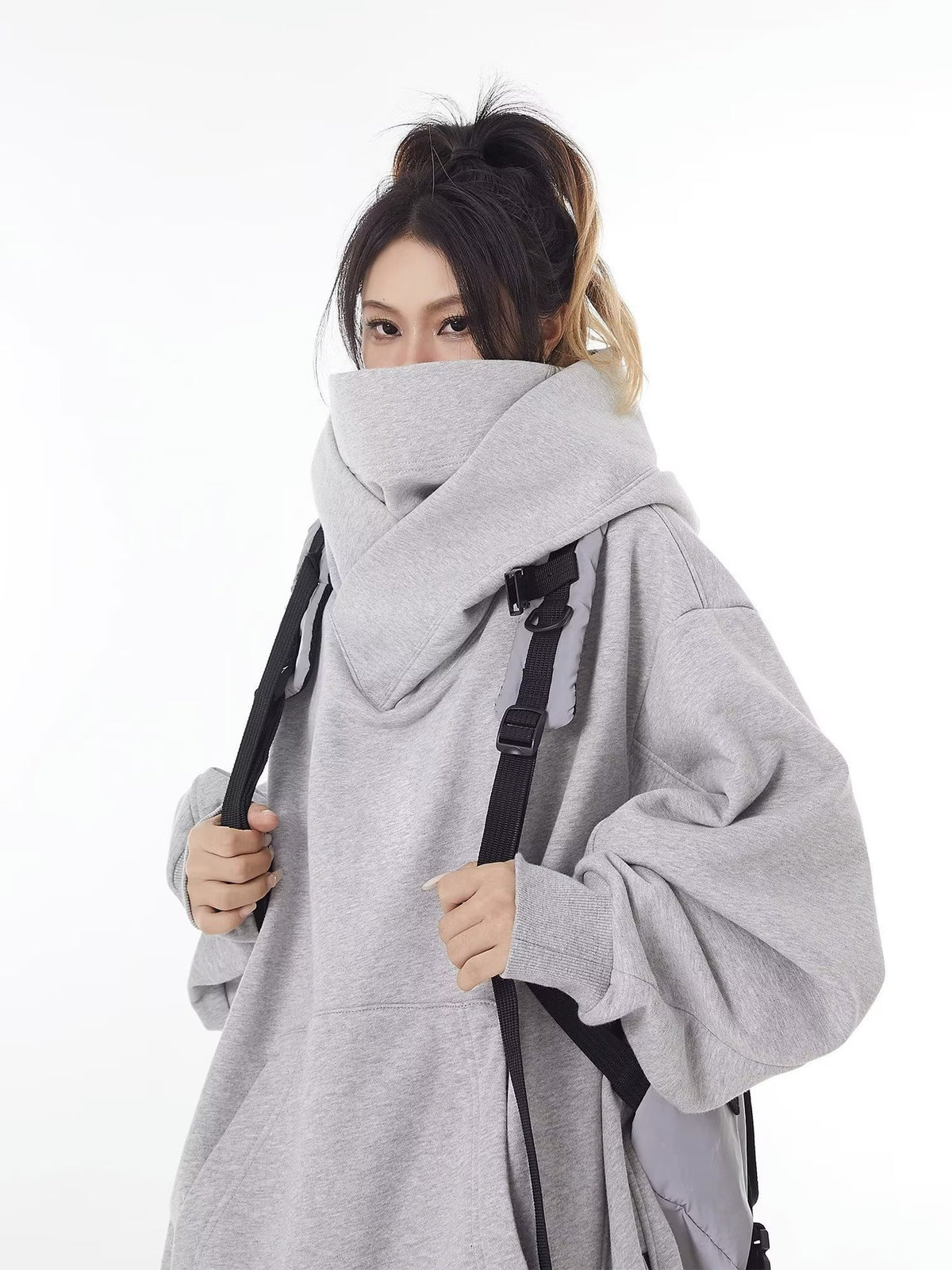 Grey oversized hooded sweatshirt with the high collar pulled up over the mouth, worn with a backpack, size option M