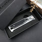 Closed folding pocket knife lying in an open black presentation box with a foam insert
