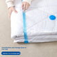 Hand sliding the zip seal closed on a clear vacuum storage bag holding a white duvet, blue valve visible