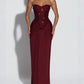 Woman in a burgundy strapless long dress with a sequin bodice and draped hip knot on a grey background