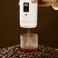 White portable espresso maker extracting a steaming shot over roasted coffee beans