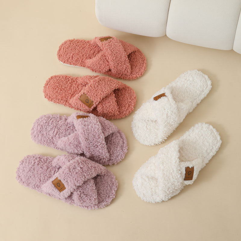Three colours of crossed plush slippers, Orange, Light purple and Beige, laid on a beige floor beside a sofa