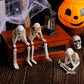 Skeleton shelf sitter figurine with legs dangling over a wooden edge