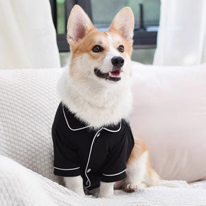 Corgi sitting on a sofa in the black pet pajama shirt with a notched collar and white piping