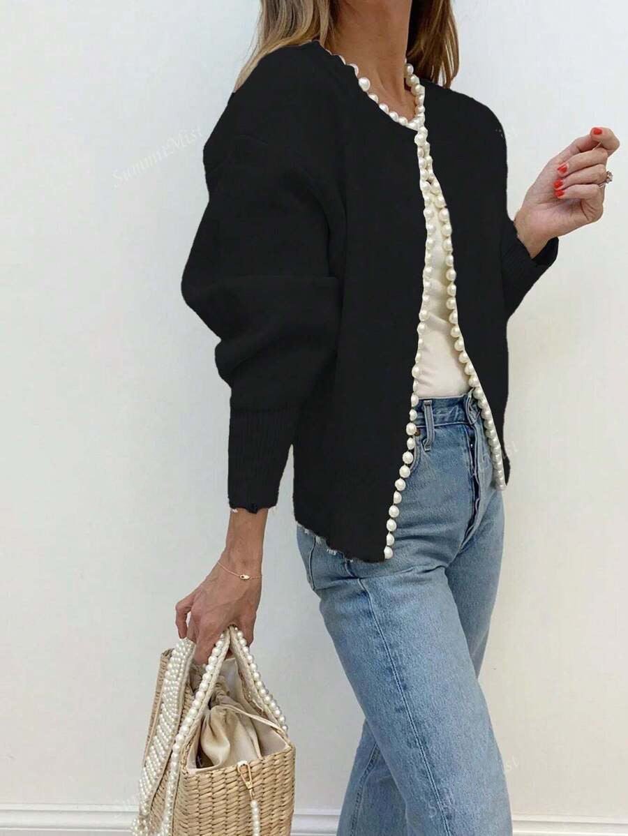 Black faux pearl trimmed knit cardigan worn open over a cream top and jeans