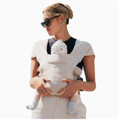Beige cotton cross-back baby carrier seen from behind showing the X straps over both shoulders