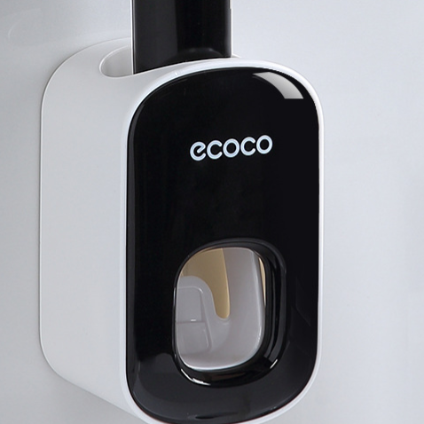 Black toothpaste dispenser mounted on a wall with a tube loaded in the top and paste at the window