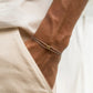 Thin gray cord friendship bracelet with a gold tone charm worn on a mans wrist