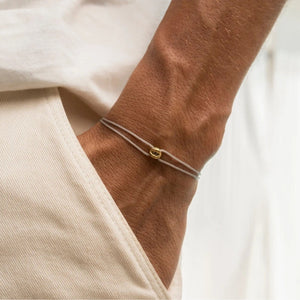 Thin gray cord friendship bracelet with a gold tone charm worn on a mans wrist