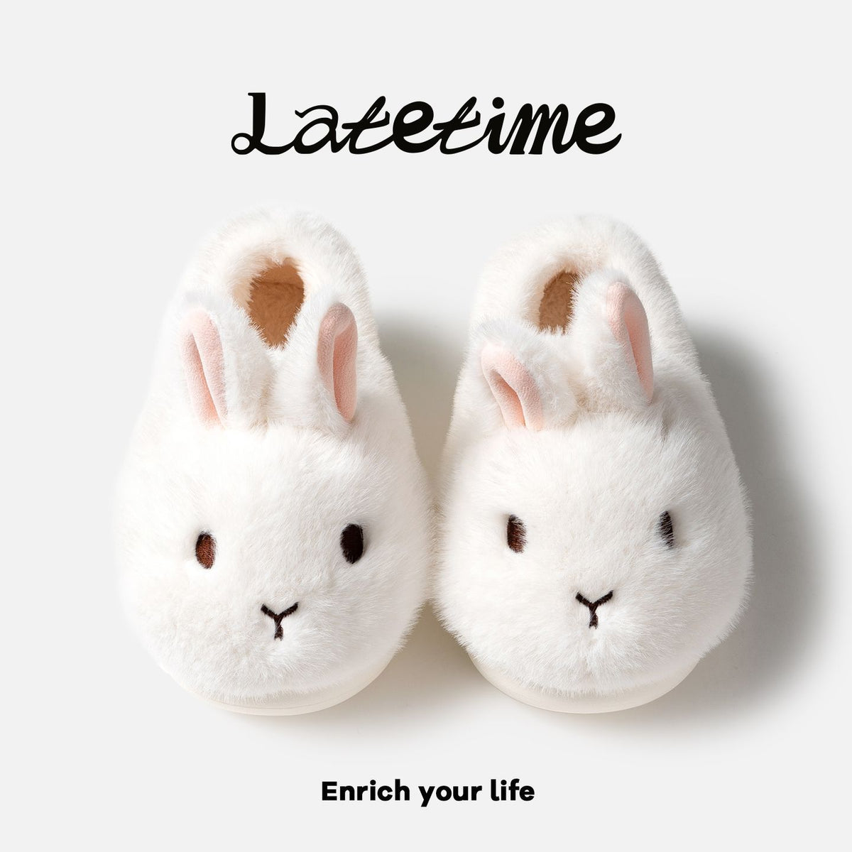 Pair of white bunny plush slippers with pink inner ears seen from above on a light panel with script lettering, view 1 of 3