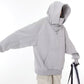 Grey hooded sweatshirt with the hood up and one arm extended, showing the front pocket and ribbed hem, cream cargo trousers