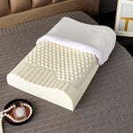 Contoured cream latex pillow on a bed with the white cover pulled back to show the nub surface